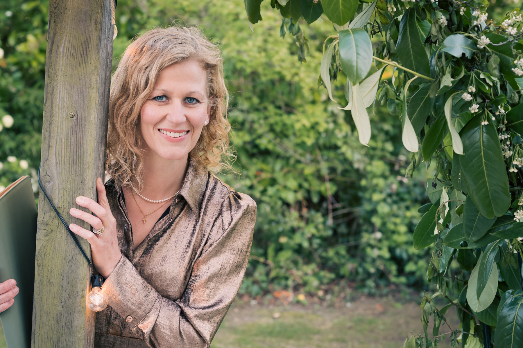 Samantha Hutchins smiling from behind a garden post, warm and welcoming